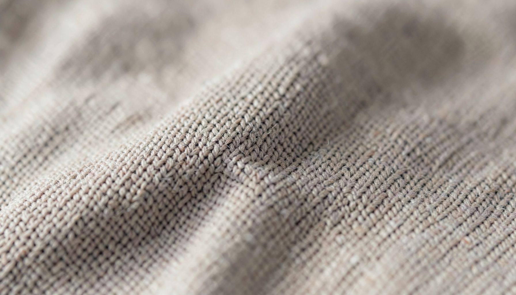 Close-up de tecido em malha de algodão em tons neutros de bege e cinza, com textura entrelaçada suave, iluminação difusa e ambiente profissional e sereno.
