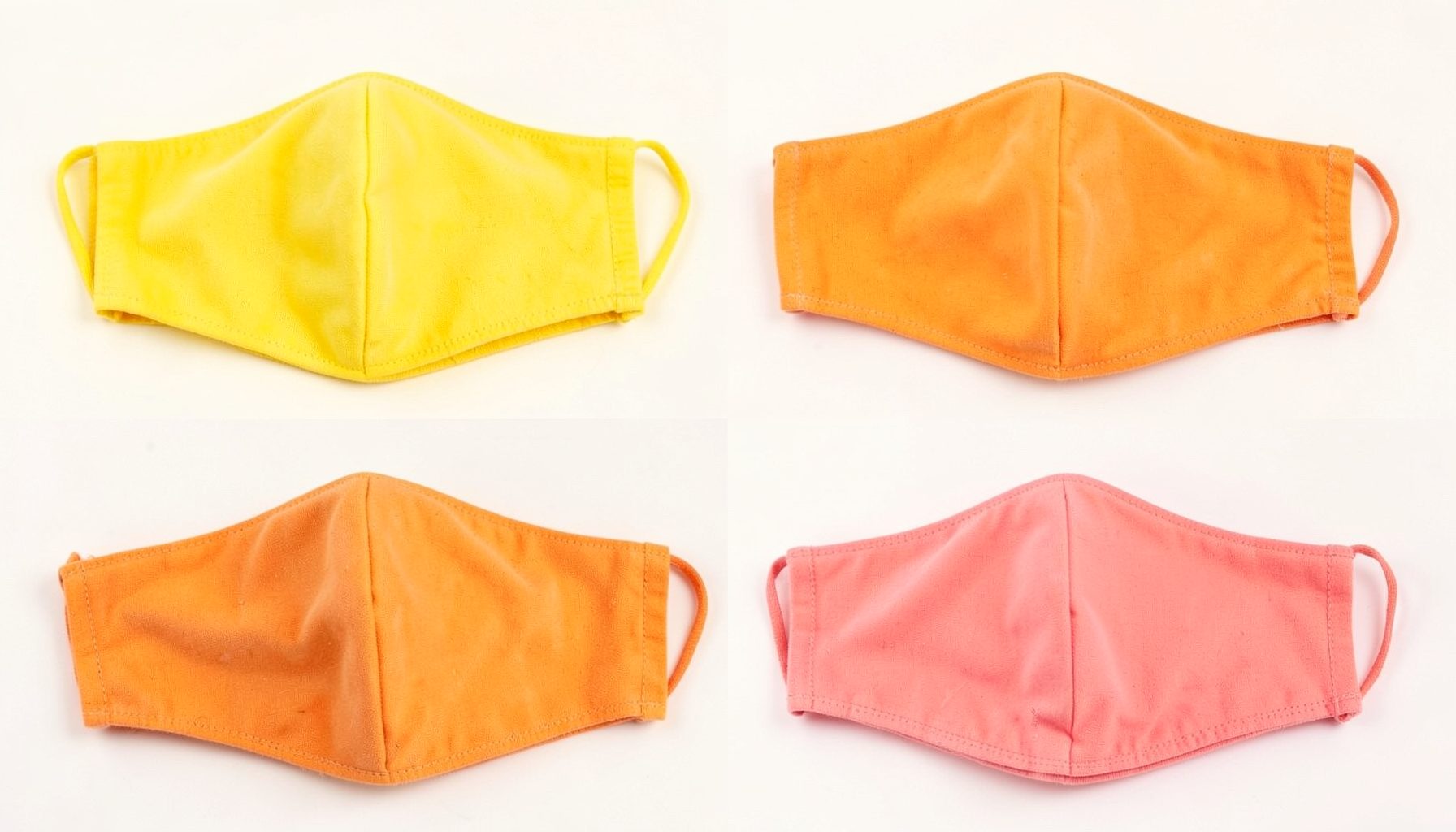 Quatro máscaras faciais de tecido em tons de amarelo, laranja e rosa dispostas sobre um fundo claro, transmitindo um ambiente alegre e acolhedor.